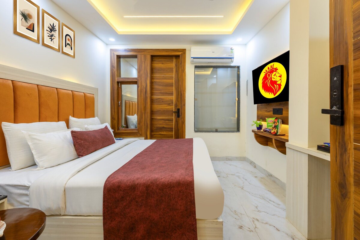 A hotel room with a bed, a TV, a wooden door, and a wall-mounted shelf with items.