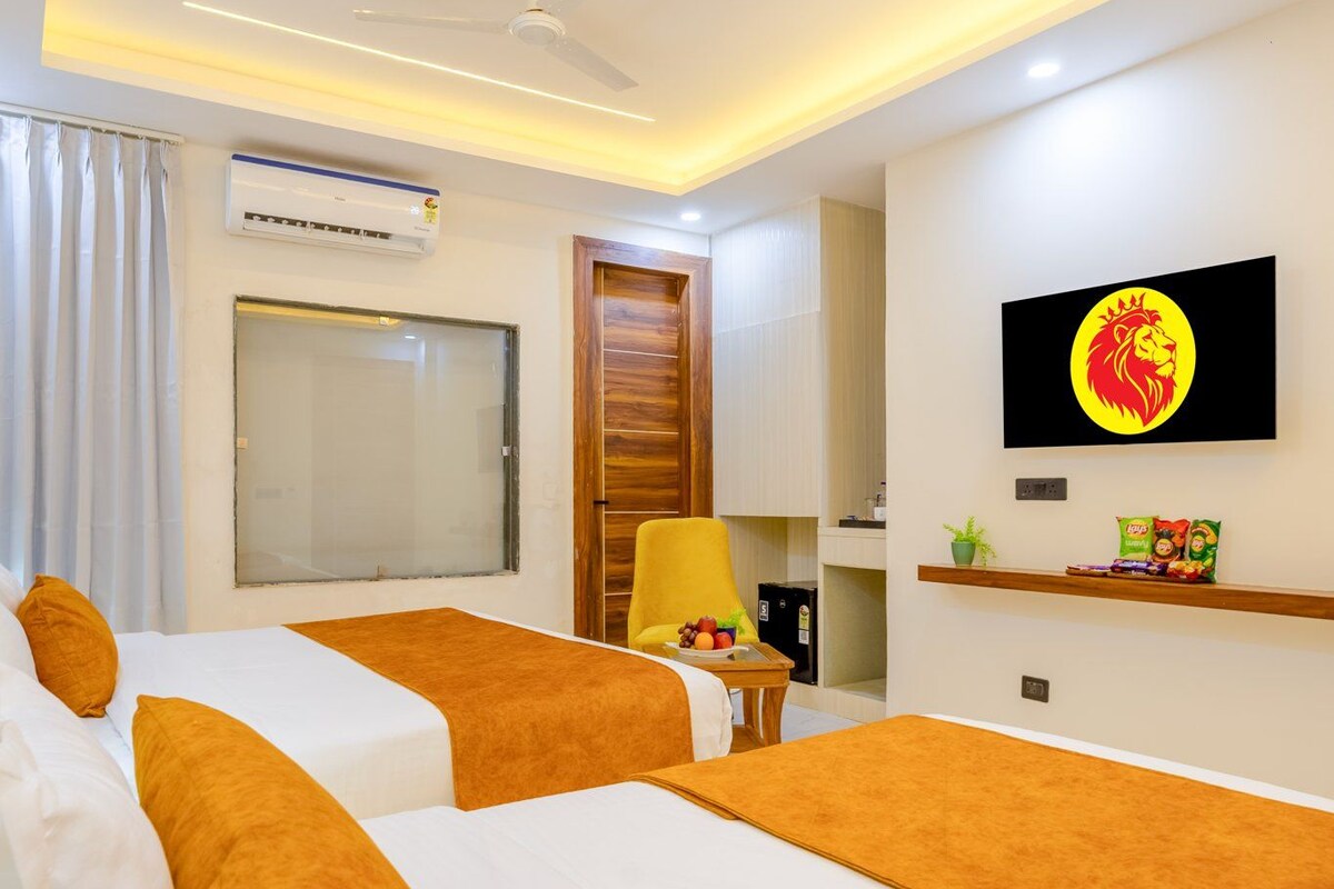A hotel room with two beds, a ceiling fan, an air conditioning unit, a television, a wooden door, and a window with curtains.