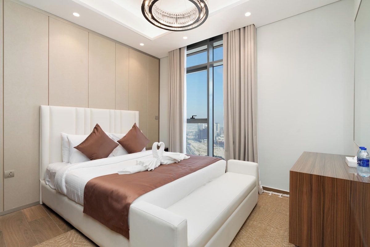 Ein modernes Hotelzimmer mit einem großen Bett, einem Holztisch und Blick auf die Stadt durch das Fenster.