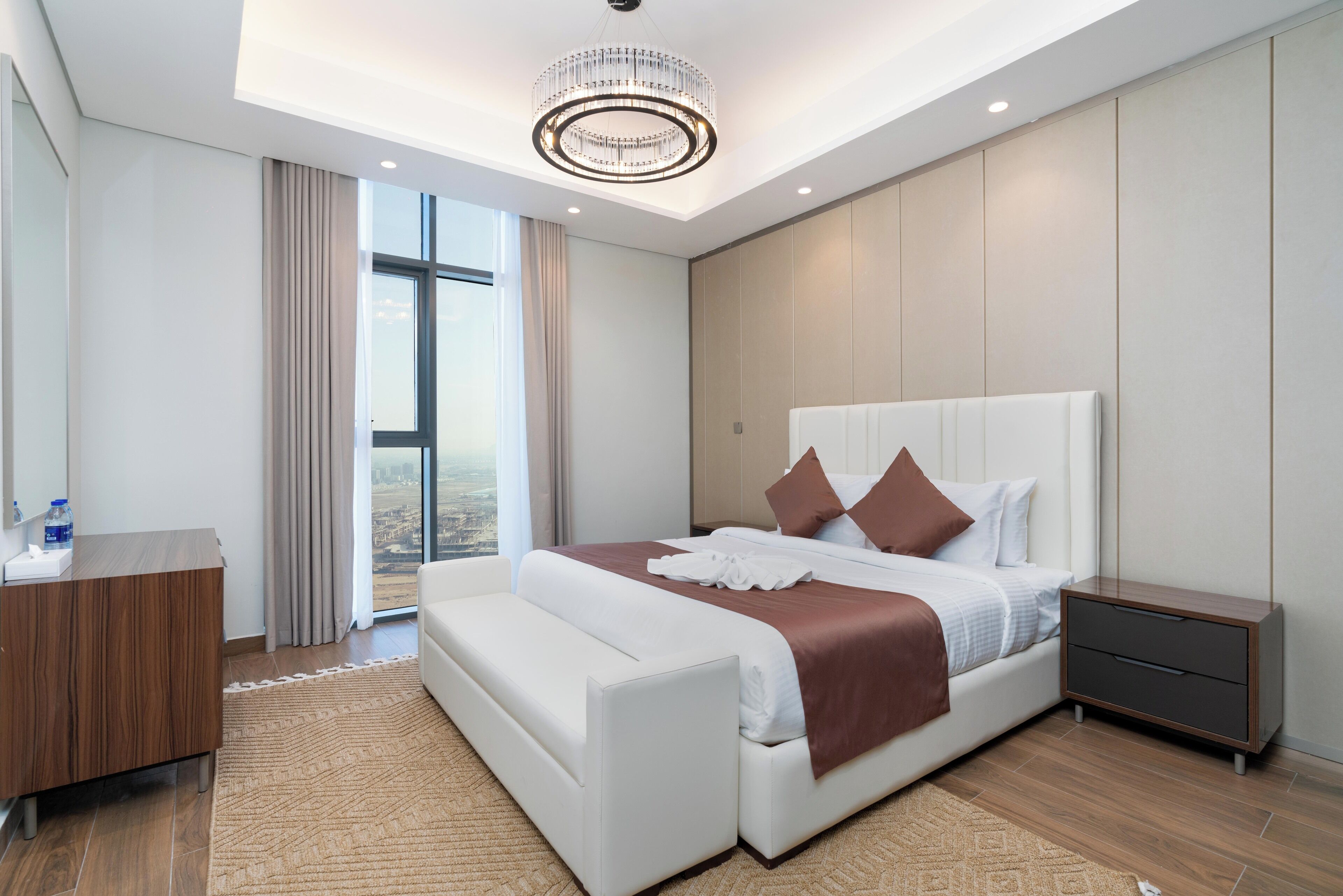A modern hotel room with a large bed, a bedside table, a nightstand, and a view of the city.
