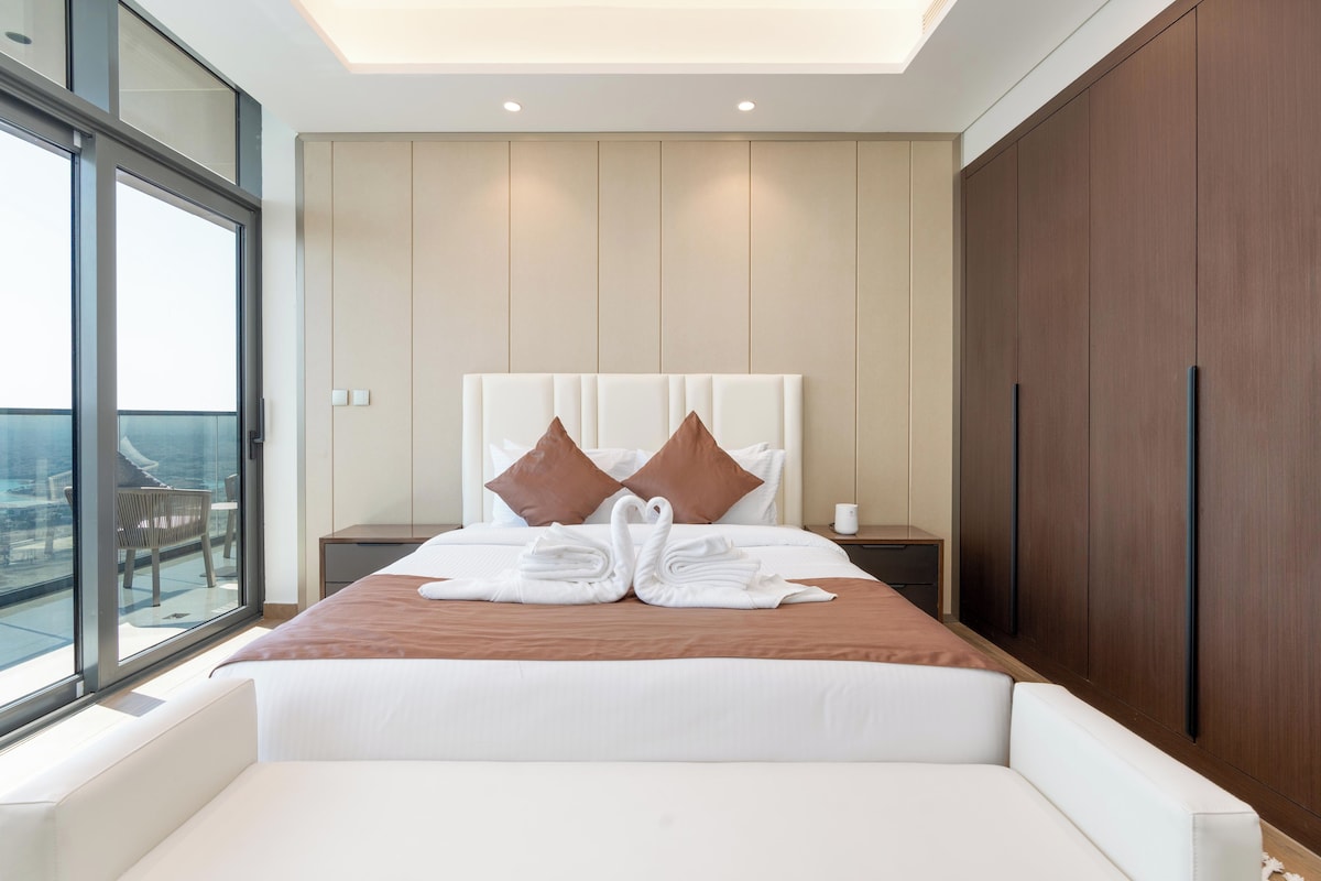 Une chambre d’hôtel moderne avec un grand lit, une table de chevet, une armoire en bois et un balcon avec vue.