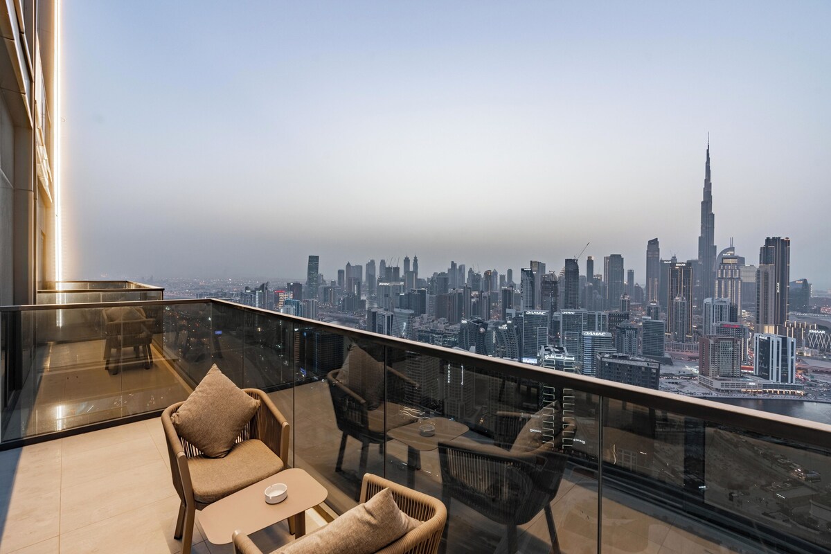 Une chambre située dans un immeuble de grande hauteur, dotée d’un balcon en verre donnant sur le paysage urbain, avec un mobilier moderne et une vue imprenable sur les gratte-ciel.