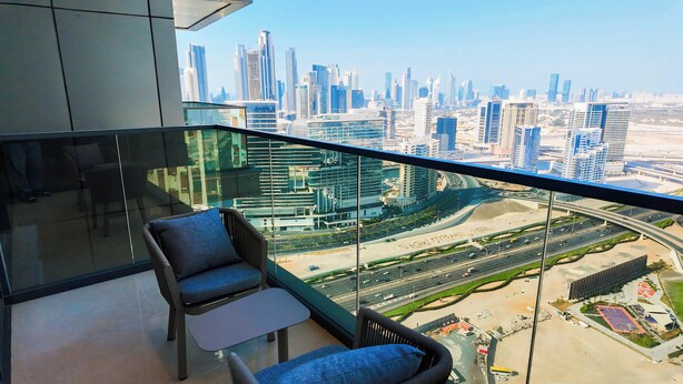 Un balcon doté d’une balustrade en verre, offrant une vue sur un paysage urbain avec de modernes gratte-ciel.
