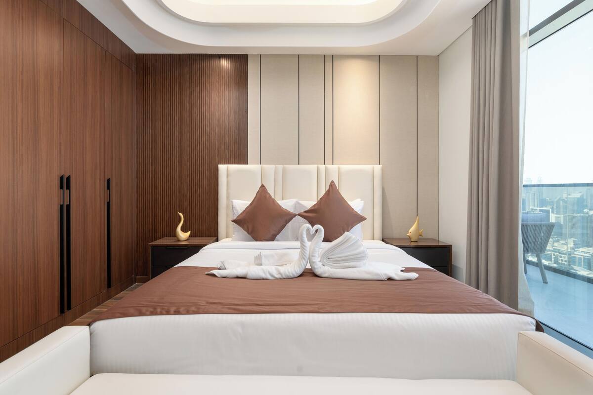 Habitación de hotel moderna con una cama grande, dos mesitas de noche, un armario de madera y vistas a la ciudad.