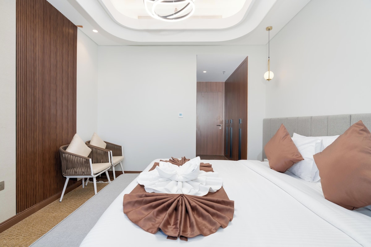 Ein modernes Hotelzimmer mit einem ordentlich bezogenen Bett, einer Sitzecke mit einem Sessel und einer Wand aus Holzpaneelen.