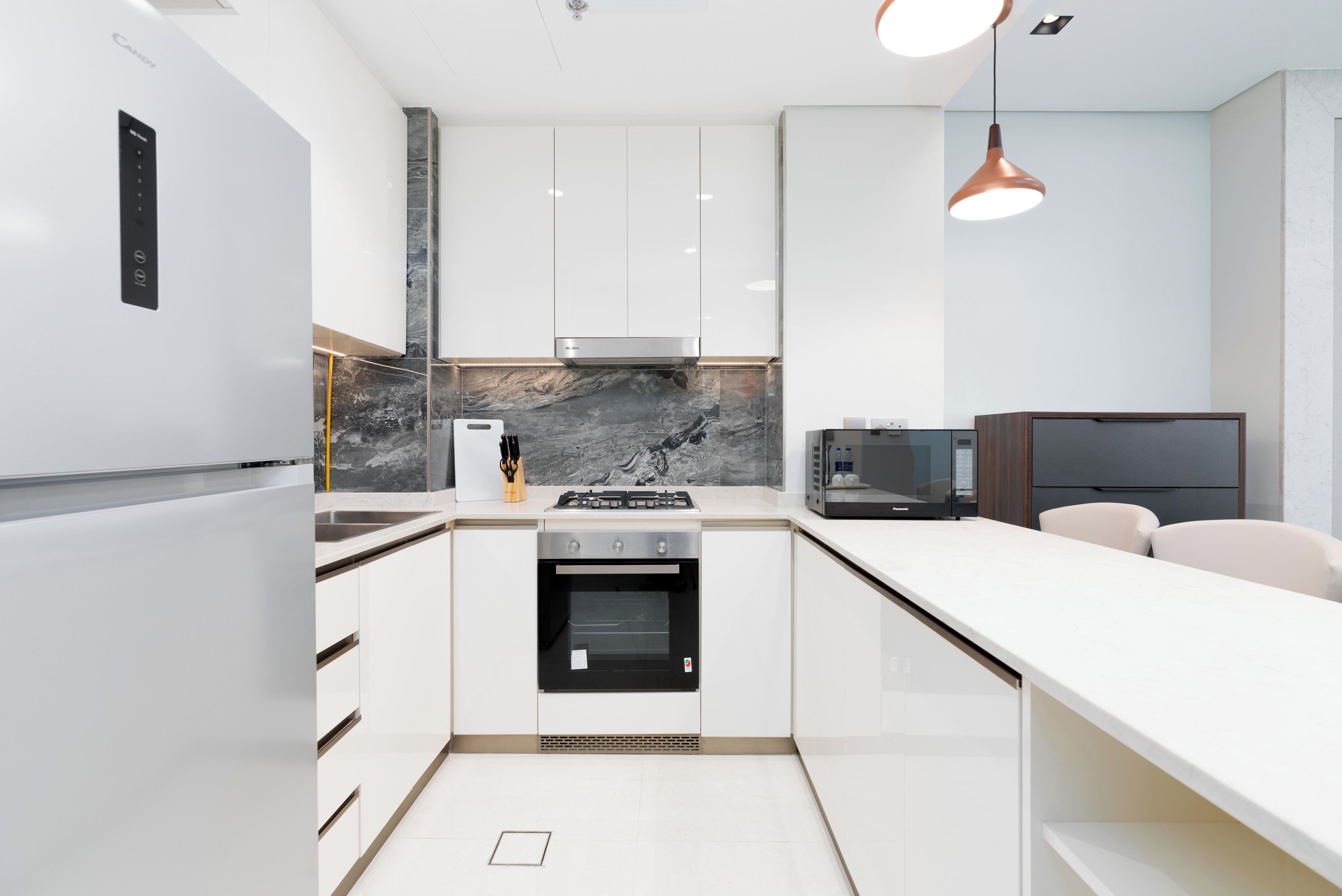 Eine moderne Küche mit weißen Schränken, einem eingebauten Backofen, einem Herd und einer Marmor-Spritzschutzwand.