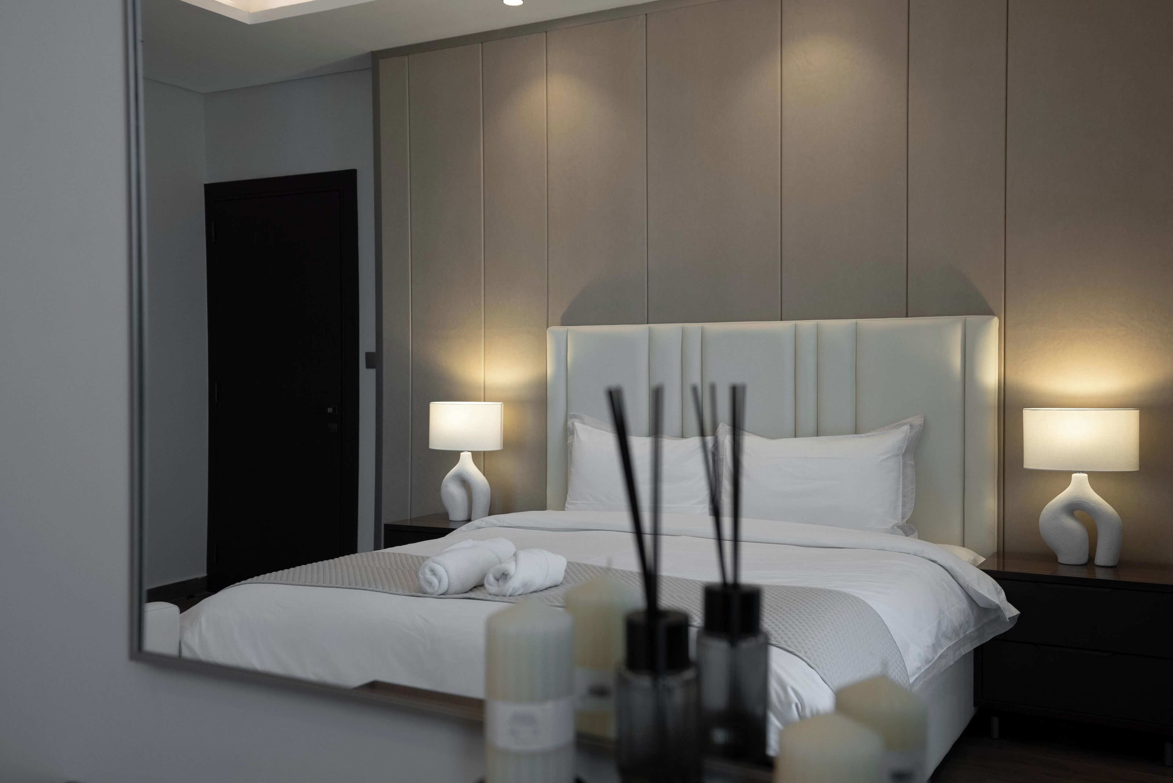 A modern hotel room with a large bed, two bedside lamps, a nightstand, and a mirror.