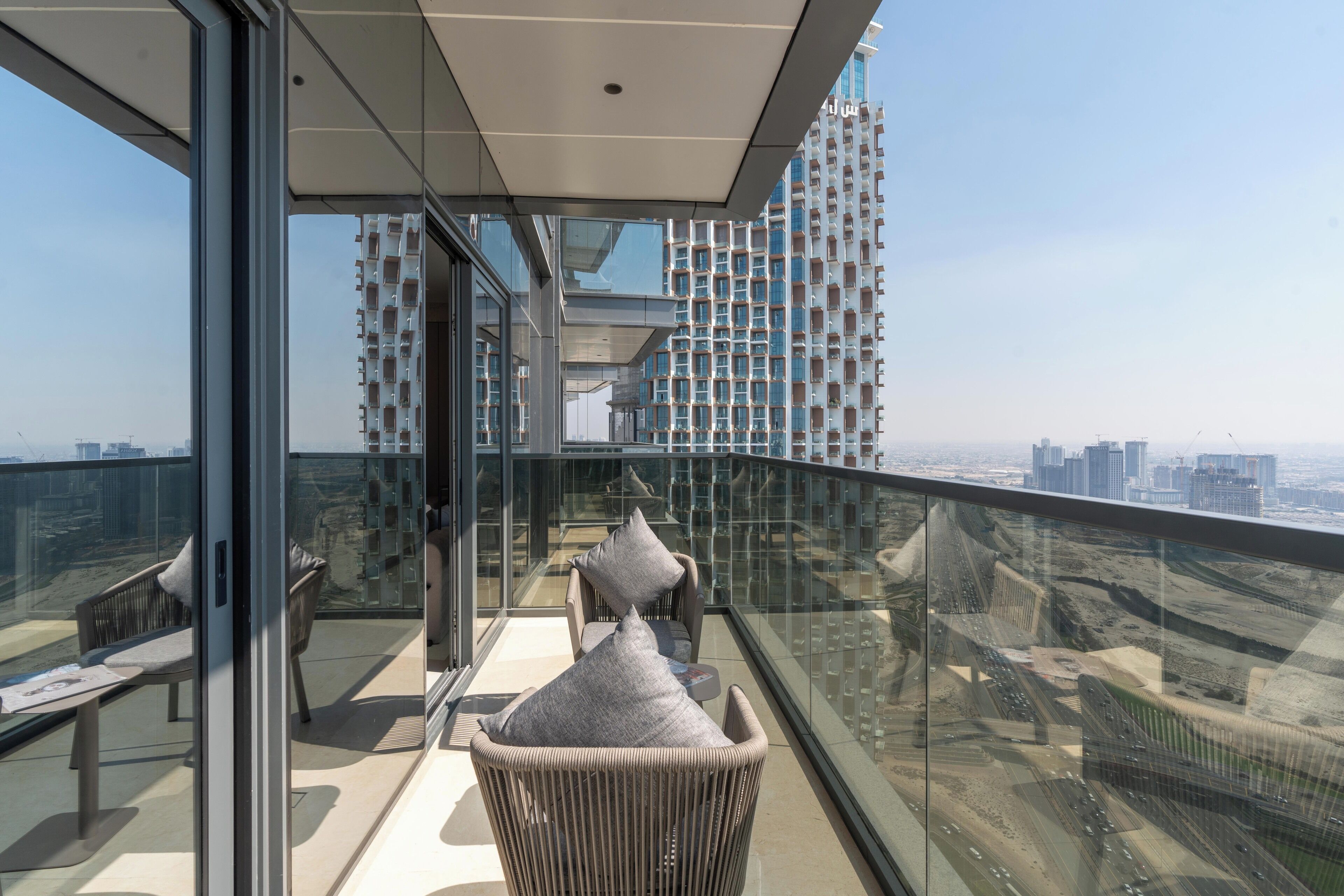 A modern balcony with glass railings, a wicker chair, and a bench.