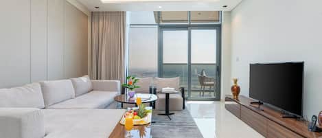 A modern living room with a sofa, coffee table, and TV. There is a balcony with a view.