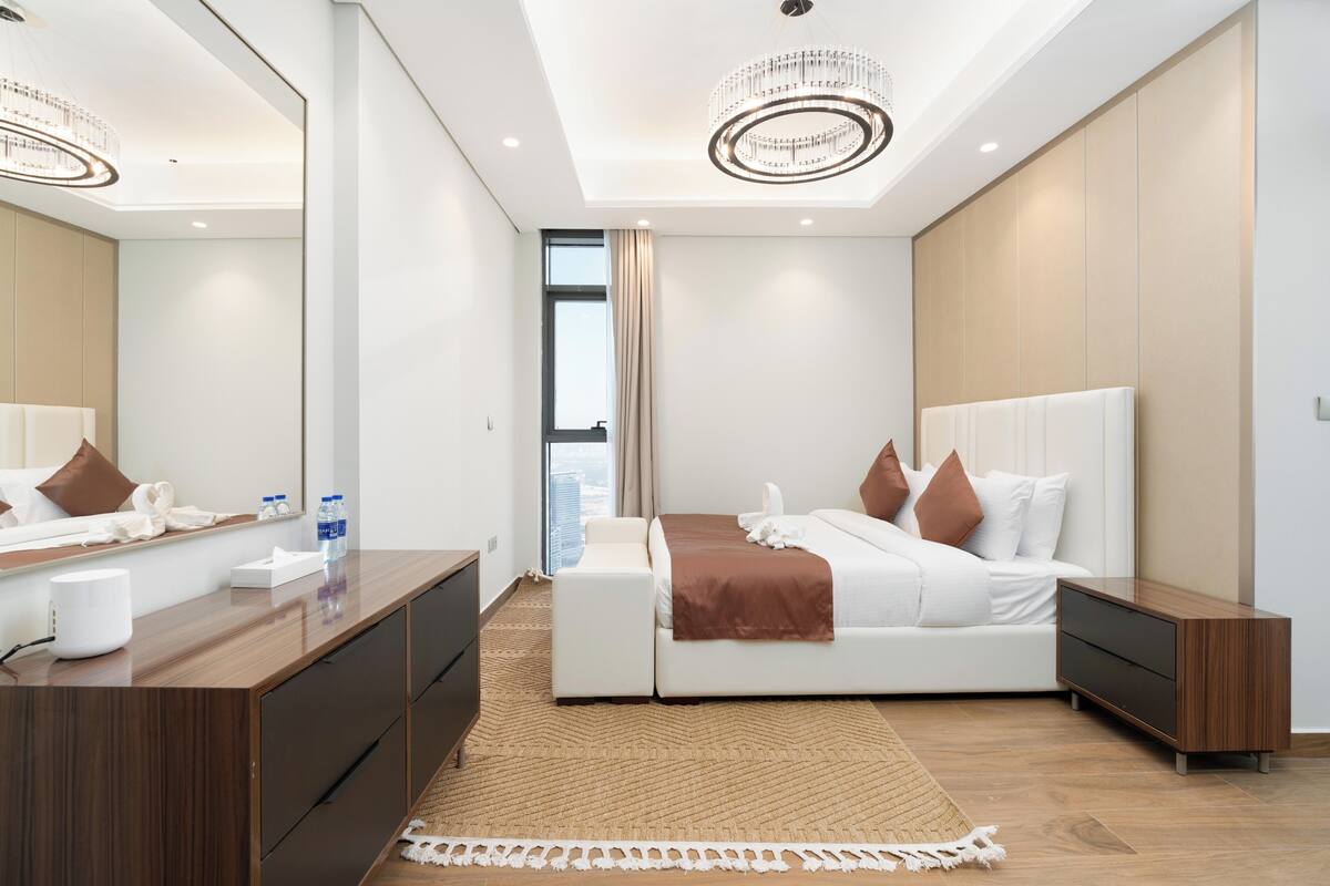 Una habitación de hotel moderna con una cama grande, una mesita de noche, un aparador y un espejo amplio.