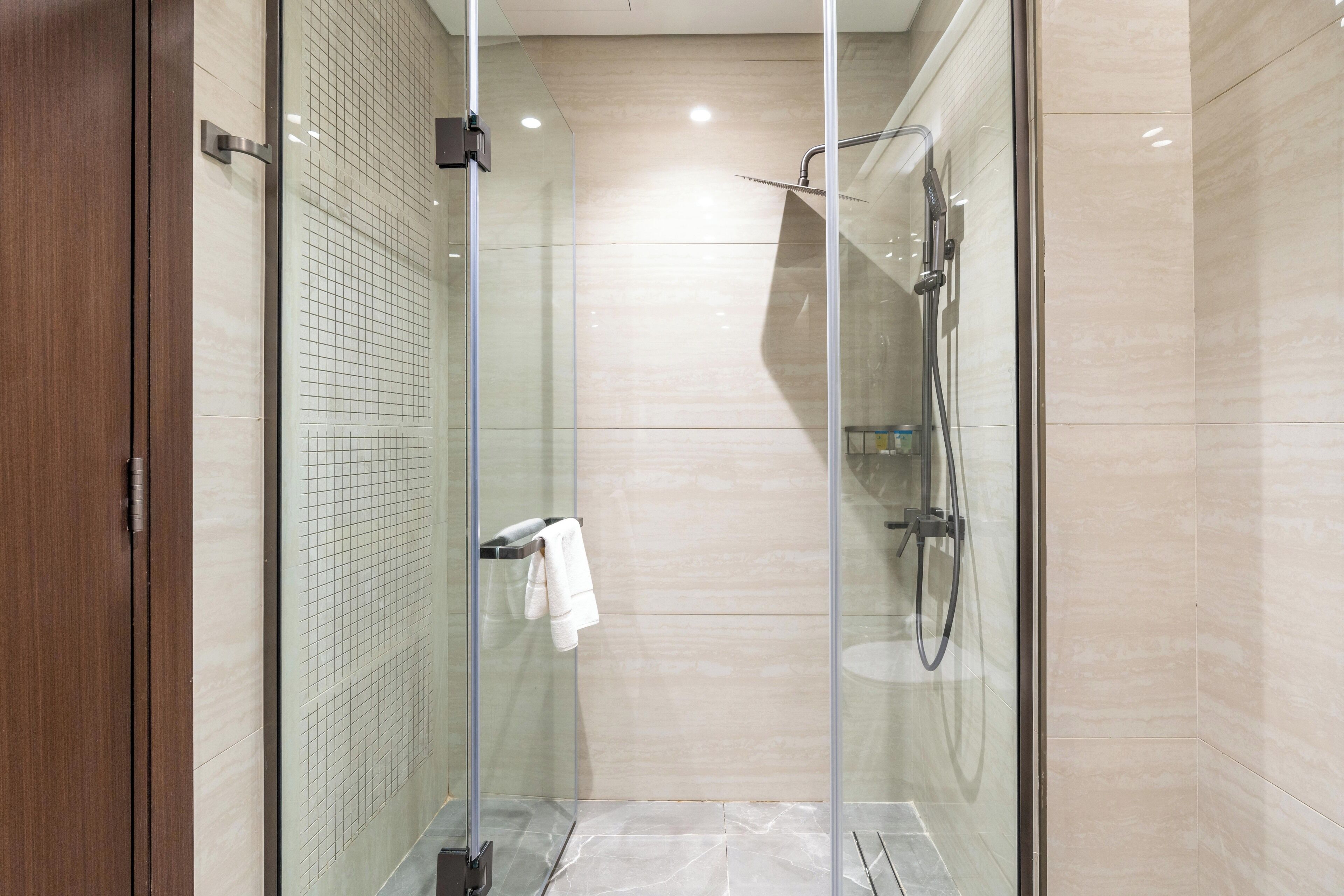 A modern shower with glass doors, a towel rack, and a marble floor.