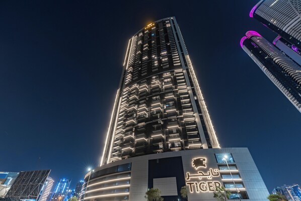 Un immeuble de grande hauteur doté de balcons illuminés et d’une enseigne bien visible sur laquelle on peut lire « TIGER ».
