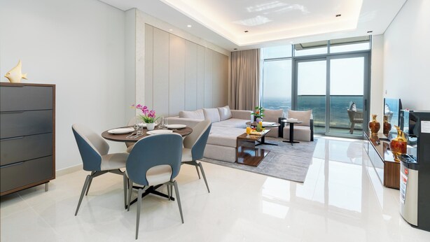 A modern living room with a dining area, a sofa, and a large window offering a view. - Samaya Holiday Homes Dubai Luxury Suites (Dubai)