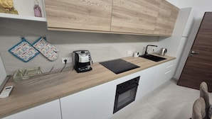 A modern kitchen with wooden cabinets, a built-in oven, a coffee maker, and a sink. - Su Cerexinu | Authentic Sardinian hospitality between Cagliari and the sea (Selargius)