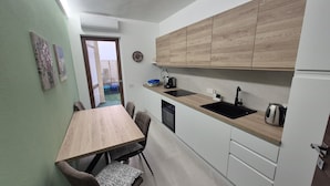A compact kitchen with a wooden countertop, a built-in oven, and a sink. There is a dining table with chairs and a patterned cushion. - Su Cerexinu | Authentic Sardinian hospitality between Cagliari and the sea (Selargius)