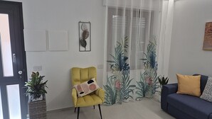 A living room with a yellow armchair, a dark blue sofa, a large window with sheer curtains, and a potted plant. - Su Cerexinu | Authentic Sardinian hospitality between Cagliari and the sea (Selargius)