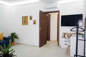 A modern room with a blue sofa, a desk with a computer, a TV, and a door leading to another room.