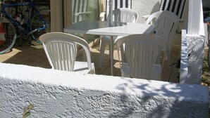 A patio with white plastic chairs and a table, a blue bicycle, and a dark blue umbrella.
