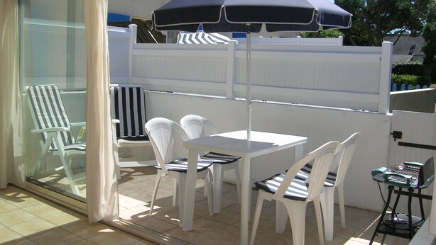 A patio area with a table and chairs, a blue umbrella, and a glass door leading to a room.