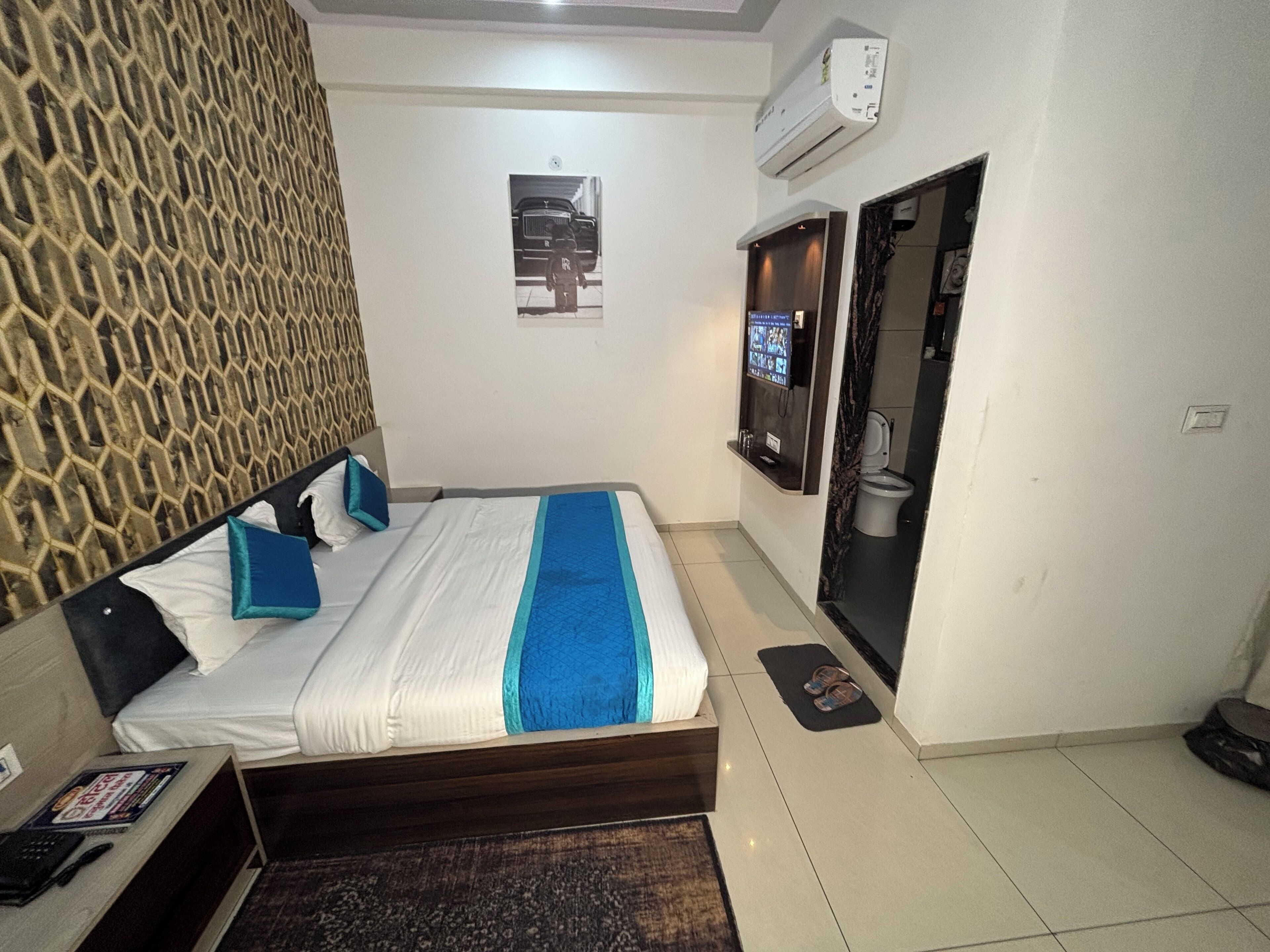 A hotel room with a bed, a TV mounted on the wall, an air conditioning unit, and a patterned wall.