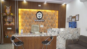 A reception desk with a logo, two bar stools, a brown sofa, and a wall with a patterned design. - Hotel Hanuman Palace (Danta Ramgarh)