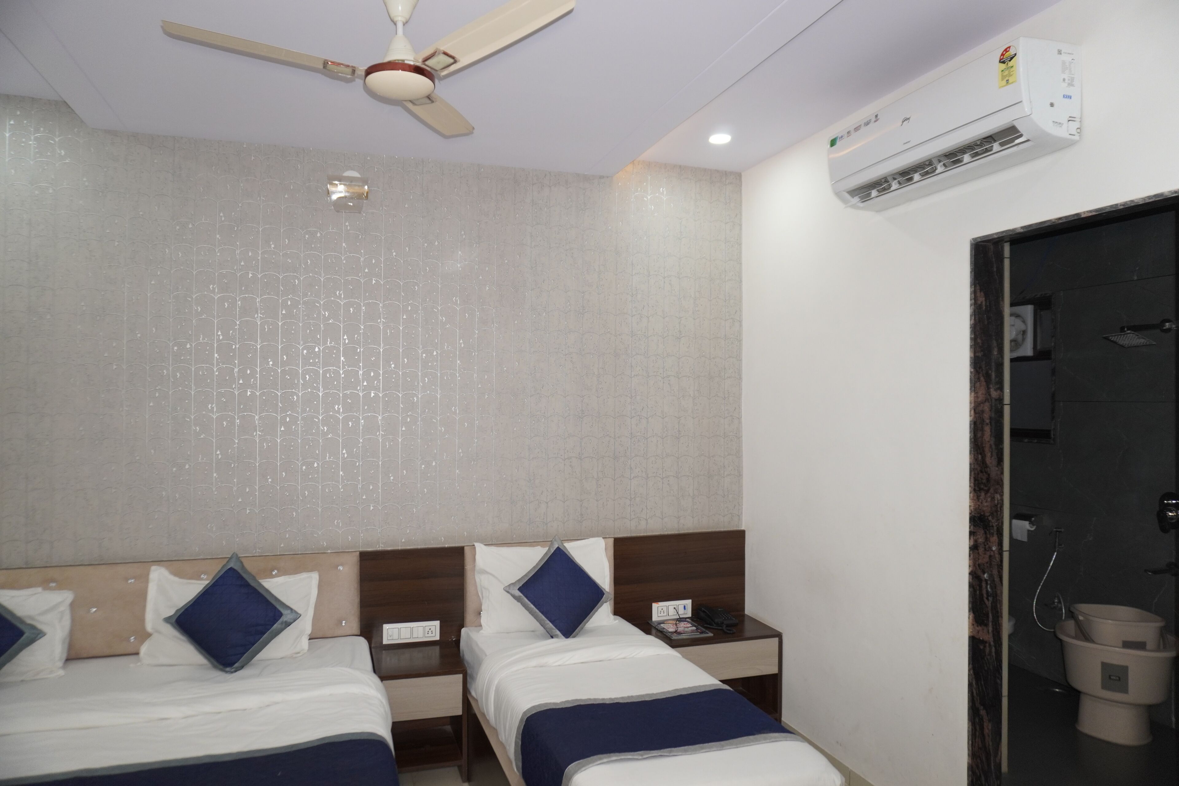 A hotel room with two beds, a ceiling fan, an air conditioning unit, and a bathroom visible through an open door.