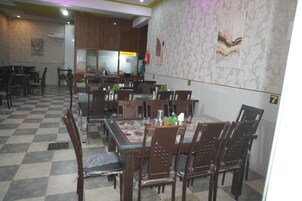 A restaurant with checkered flooring, wooden tables and chairs, and a marble wall with artwork.