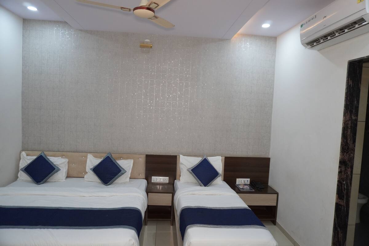Habitación de hotel con dos camas, ventilador de techo, aire acondicionado y puerta al baño.
