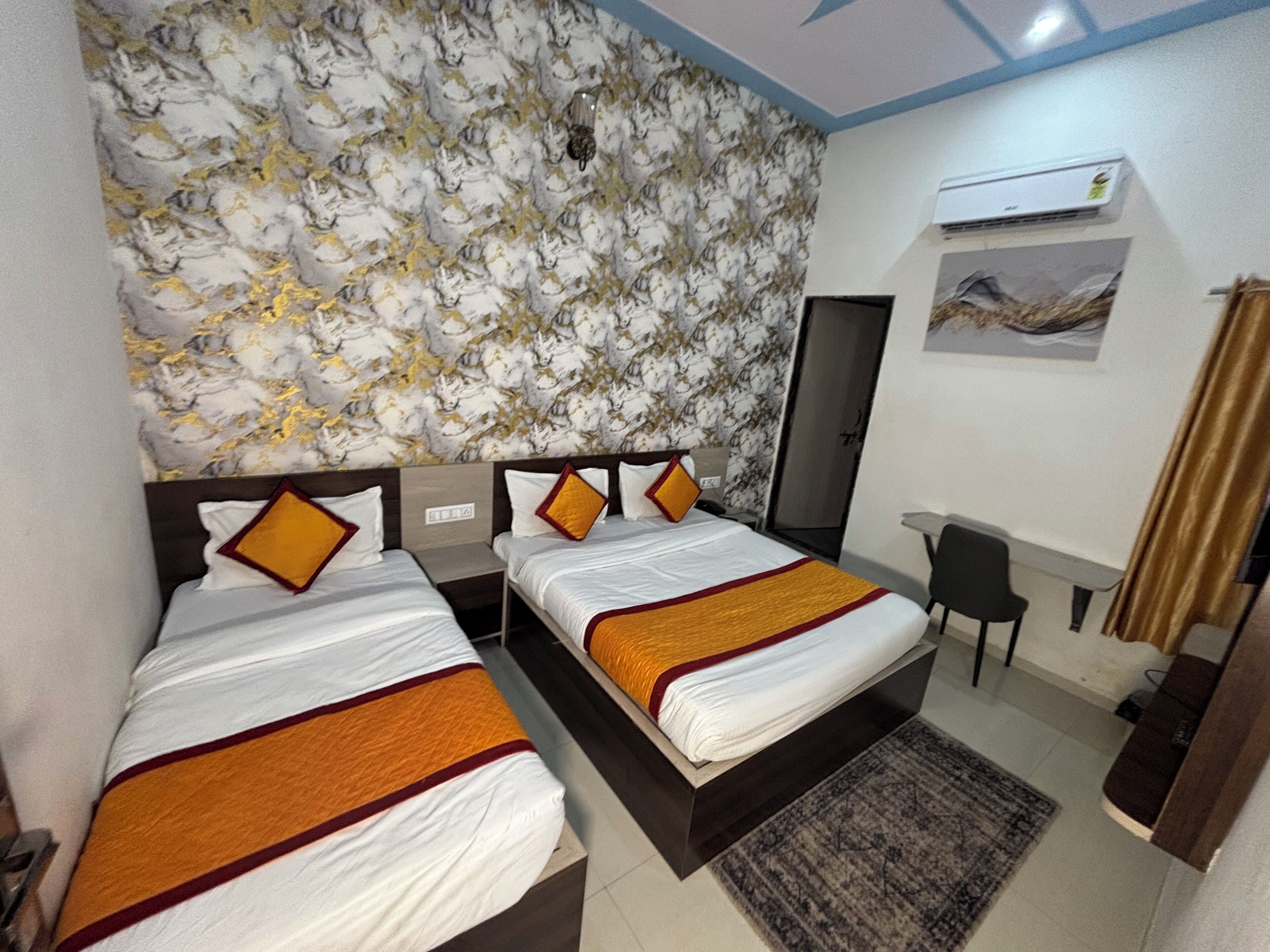 A hotel room with two beds, a desk, a chair, an air conditioning unit, and a patterned wall.