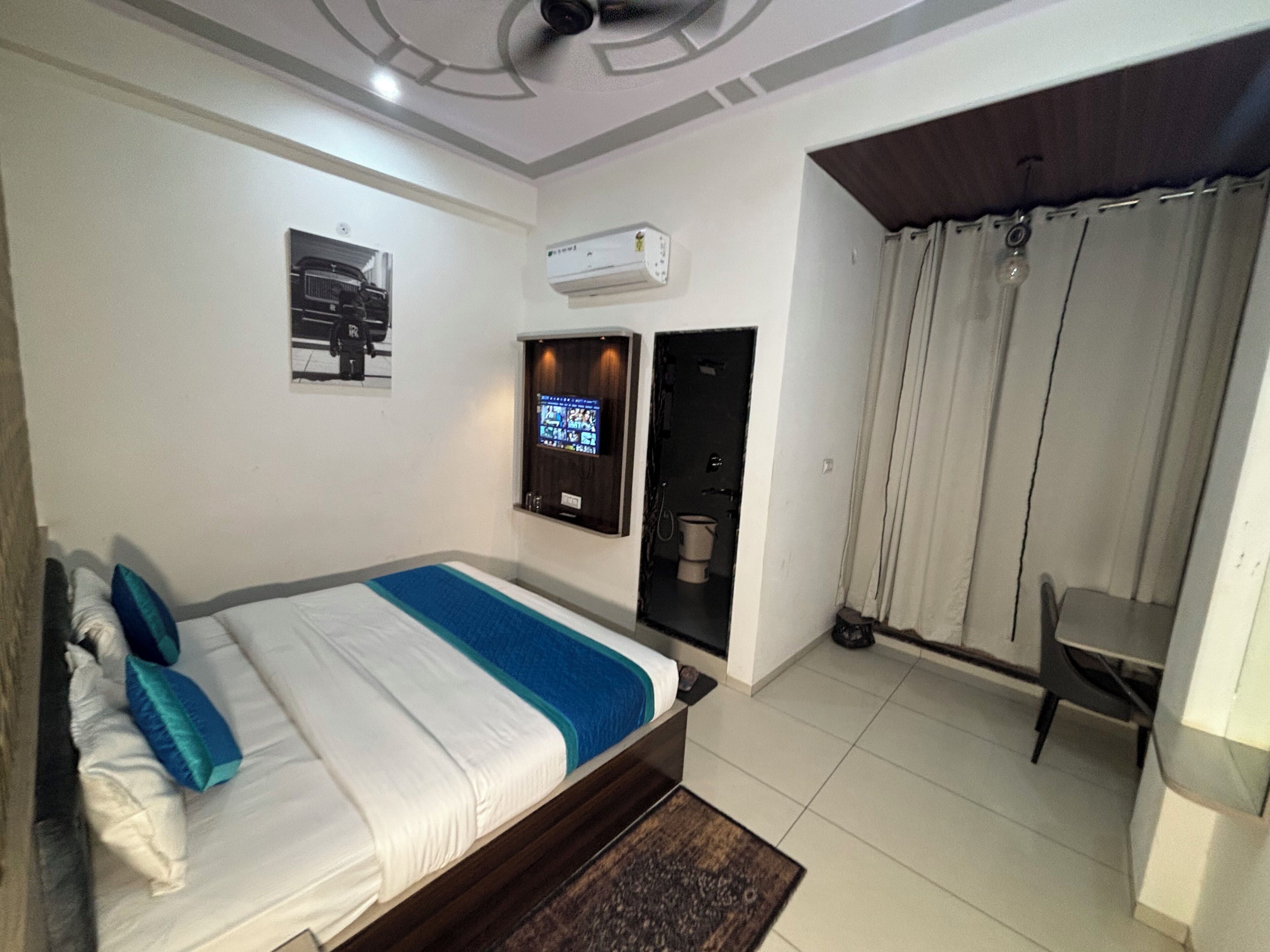A hotel room with a bed, a TV mounted on the wall, an air conditioning unit, and a view of the outside through a door.