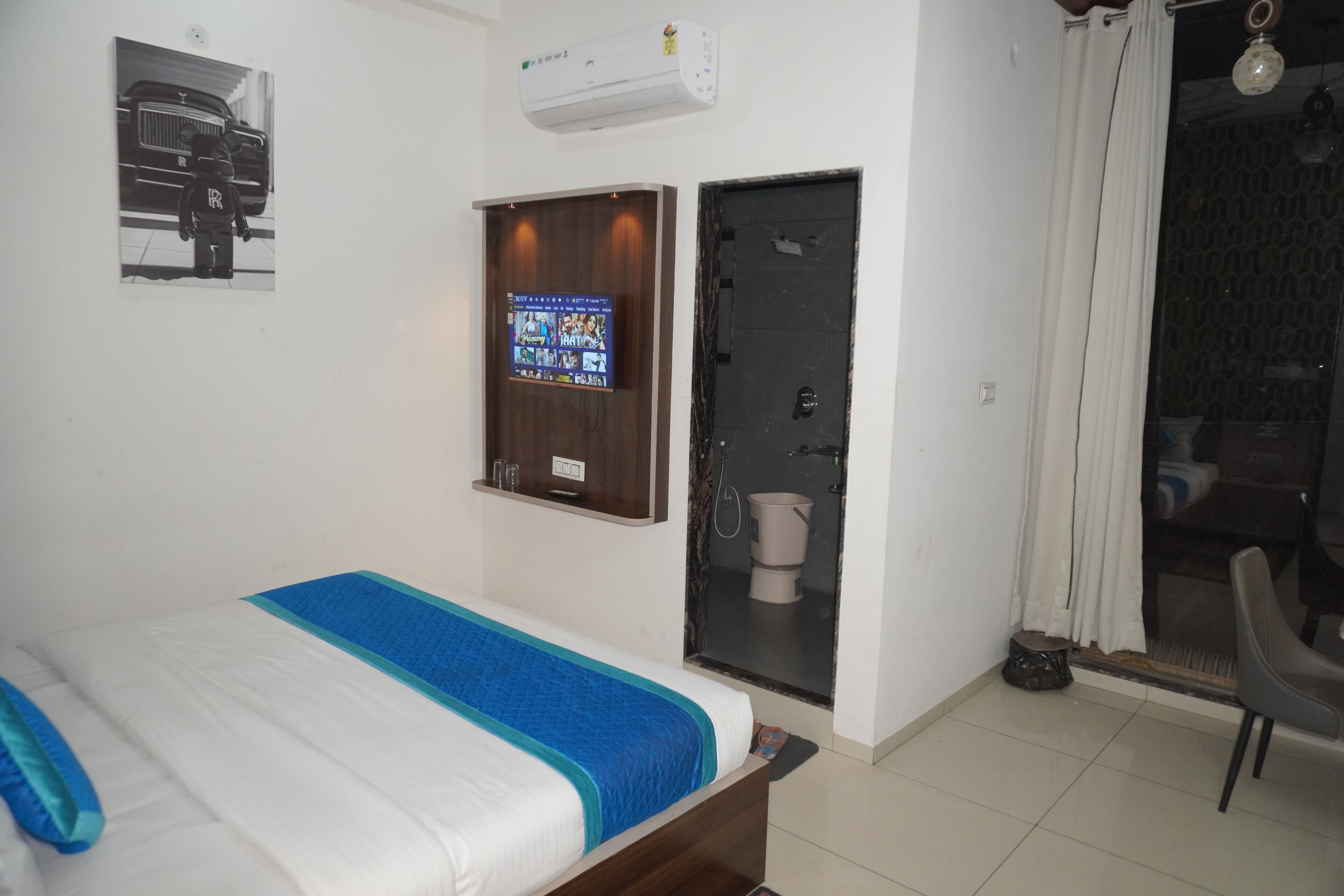 A bedroom with a bed, a TV mounted on the wall, a door, and a window with curtains.