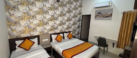 A hotel room with two beds, a desk, a chair, an air conditioning unit, and a door.