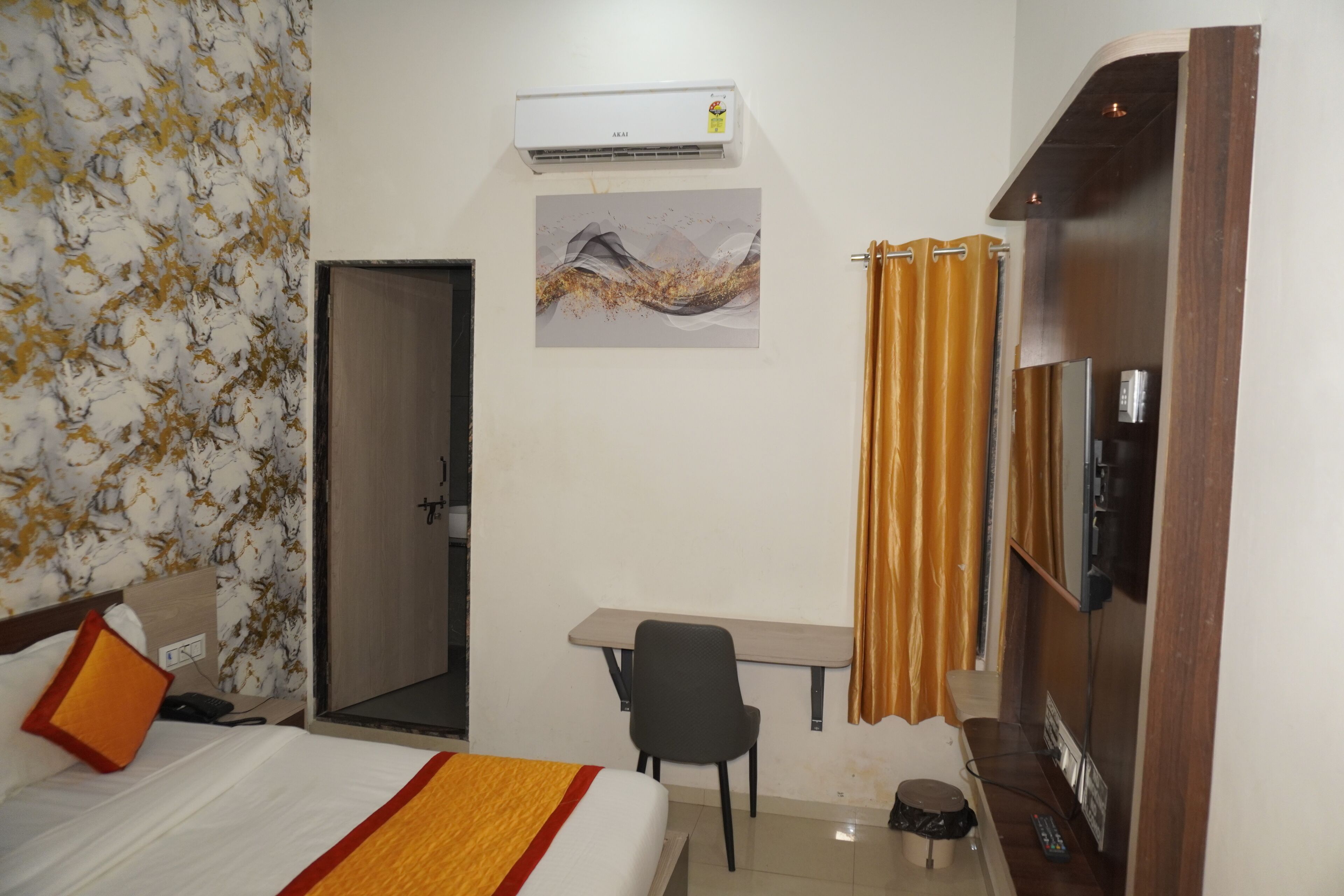 Habitación de hotel con cama, escritorio, silla, aire acondicionado, obra de arte, cortinas y televisor.