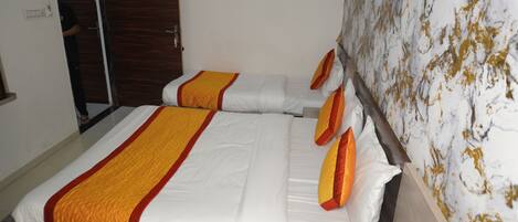 A hotel room with two beds, each with white bedding and orange accents. There is a wooden headboard and a marble-patterned wall.