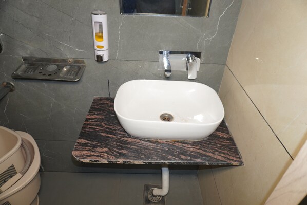 Un baño con lavamanos blanco, encimera de mármol y un espejo pequeño arriba.