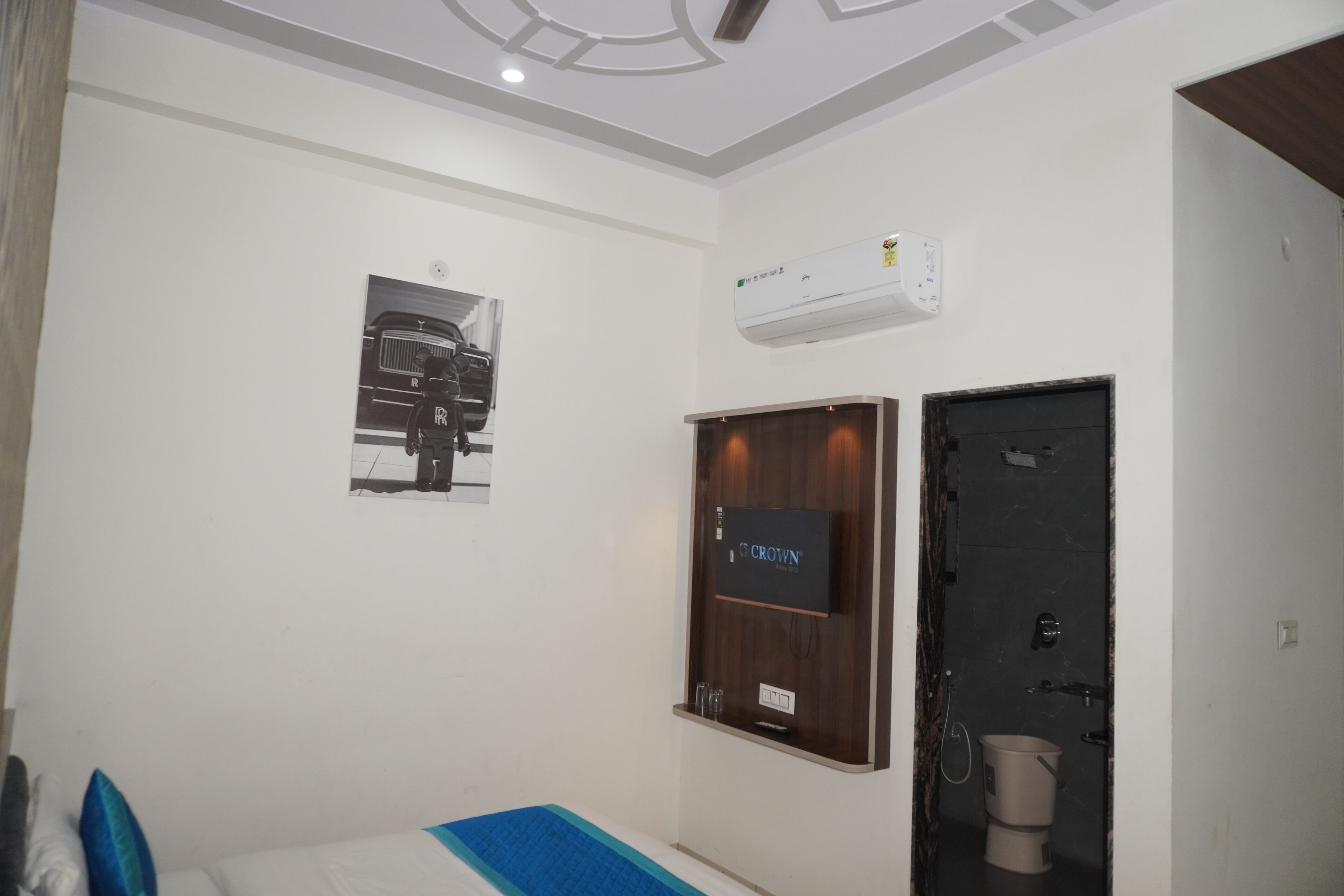 Habitación de hotel con cama, televisión montada, equipo de aire acondicionado y puerta que da a un baño.