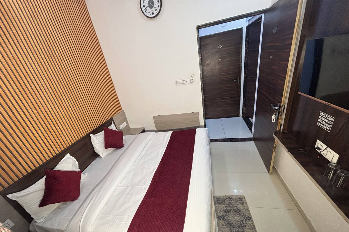 Habitación de hotel con una cama, cabecera de madera, un reloj en la pared, un mostrador de recepción y una puerta.