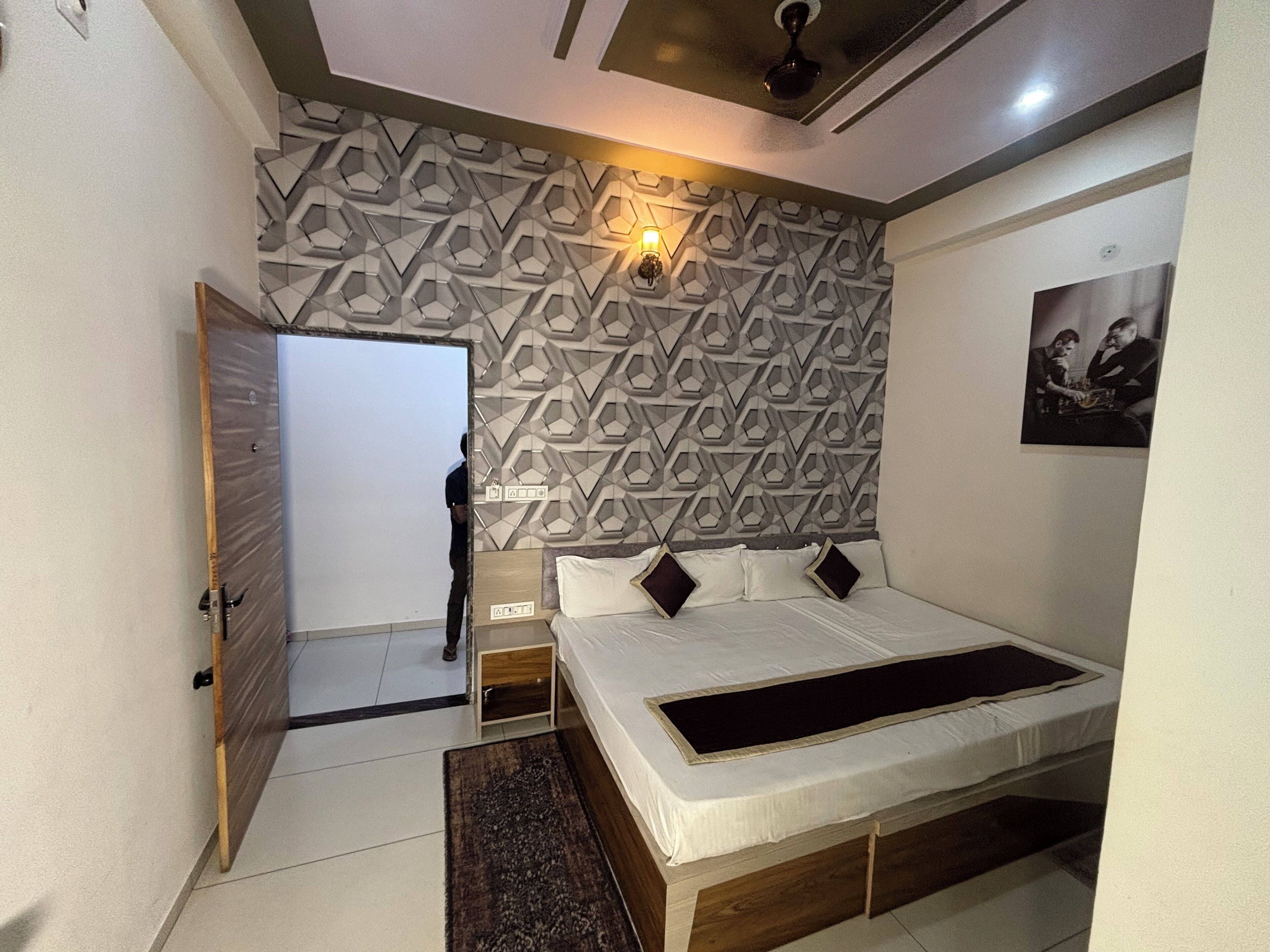Un dormitorio con pared de estampado geométrico, una cama con detalles negros, una mesita de noche y un ventilador de techo.
