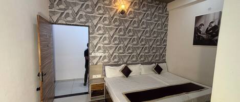 Un dormitorio con pared de estampado geométrico, una cama con detalles negros, una mesita de noche y un ventilador de techo.