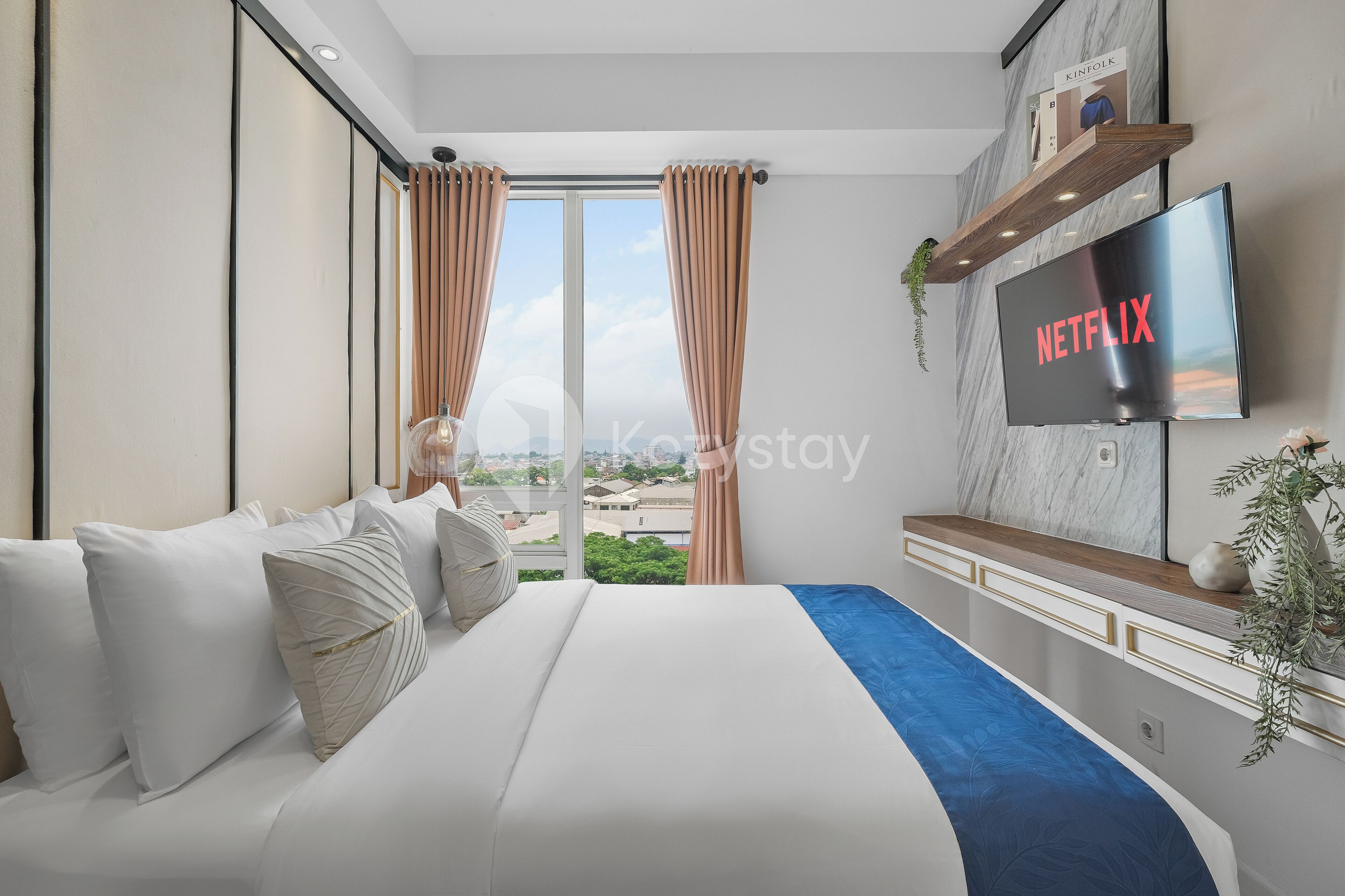 A modern hotel room with a large bed, a mounted TV displaying 'NETFLIX', a city view, and a mounted shelf with decorative items.