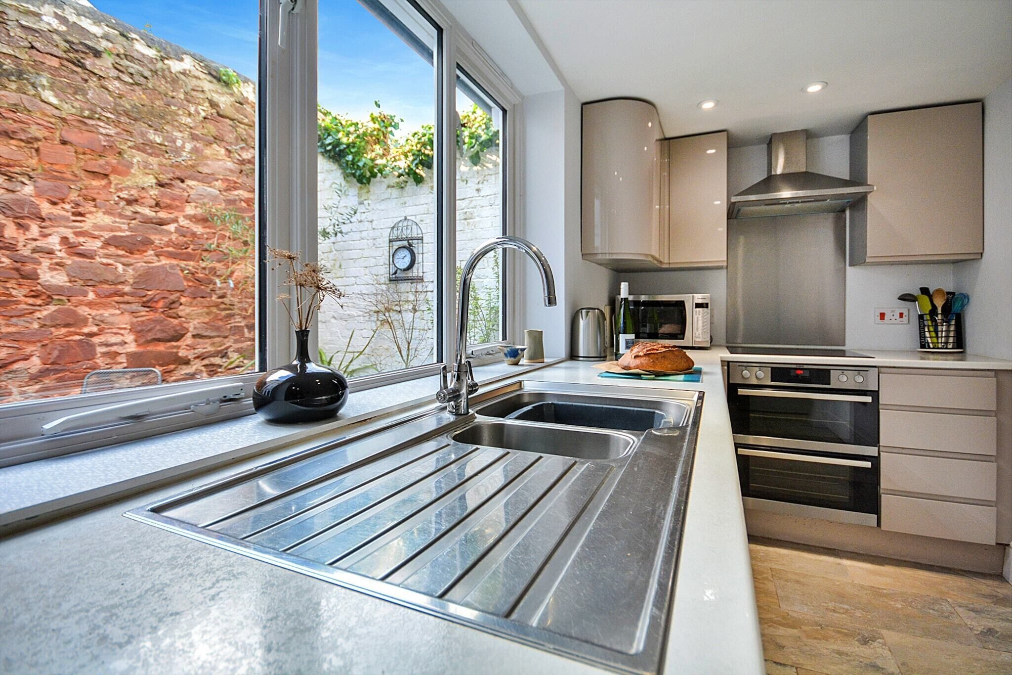 A modern kitchen with a large window, stainless steel appliances, and a stone wall outside.