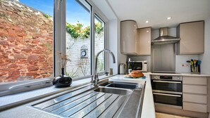 A modern kitchen with a large window, stainless steel appliances, and a stone wall outside. - Apartment in Pickering by Riverside Views (Kingsand)