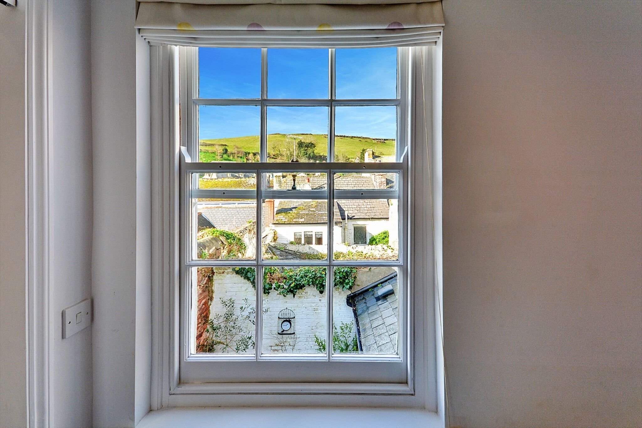 A window with a view of a town, including buildings and a hill.