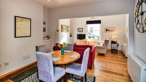 A modern living room with a wooden dining table, grey upholstered chairs, a red sofa, and a large clock on the wall. - Apartment in Pickering by Riverside Views (Kingsand)