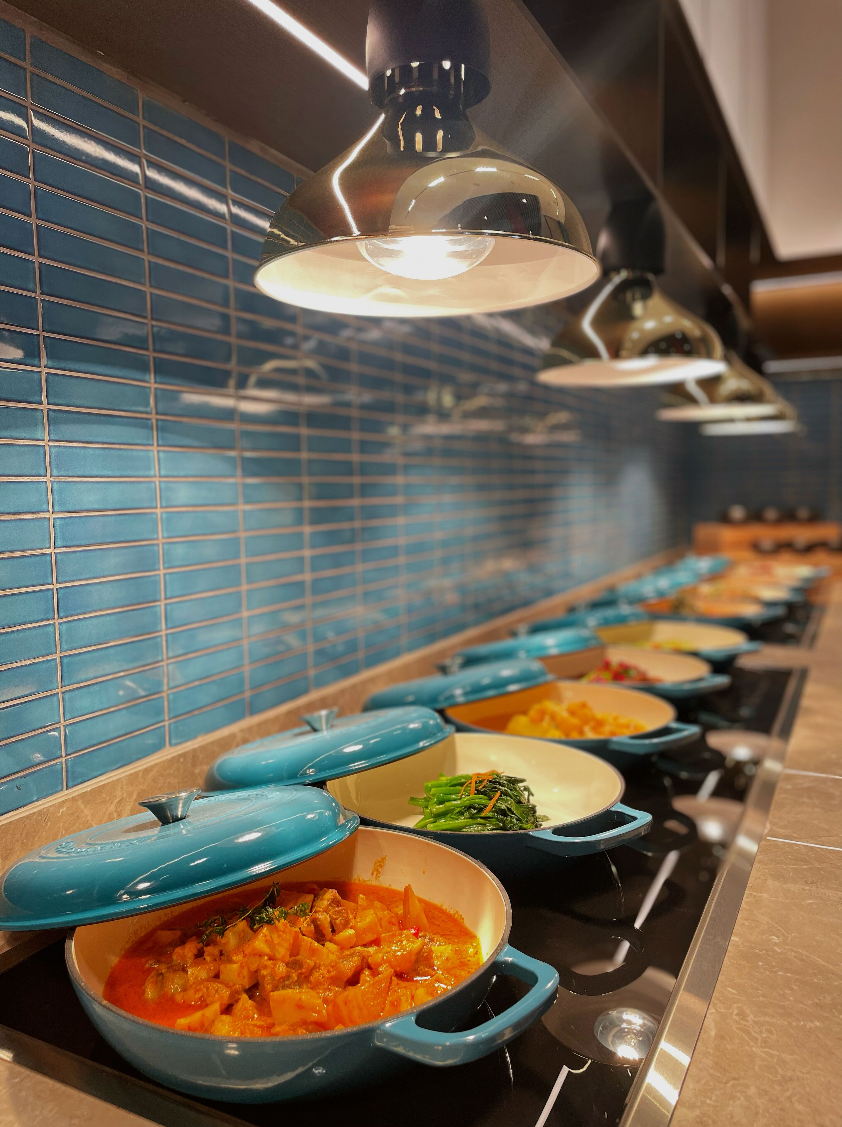 Une cuisine avec une rangée de casseroles bleues sur le plan de cuisson, un dosseret de carreaux bleus et un luminaire suspendu moderne.