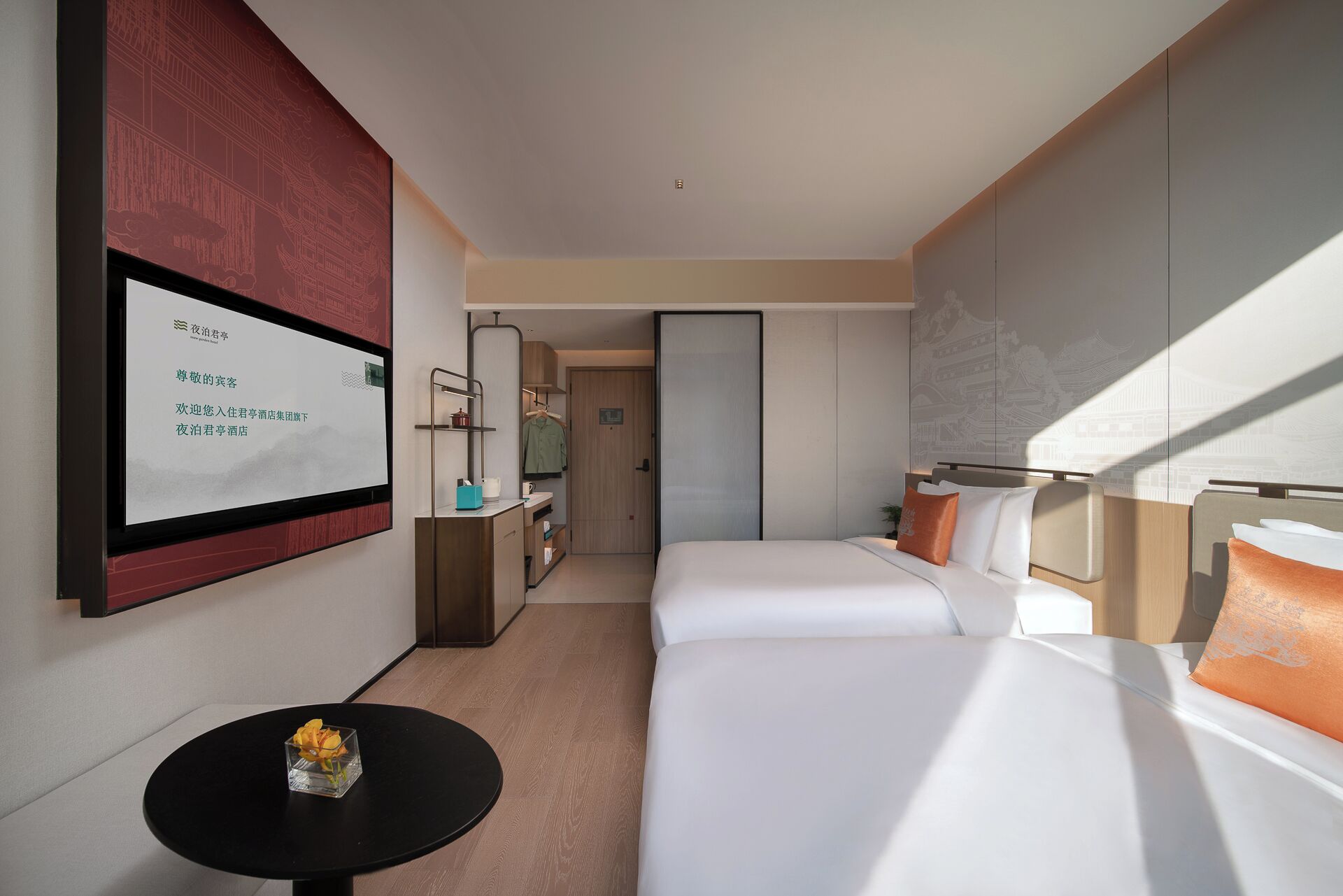 Una habitación de hotel con cama, una mesita con un florero, un espejo y un televisor en la pared.