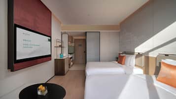 Une chambre d’hôtel avec un lit, une petite table sur laquelle est posé un vase, un miroir et un téléviseur fixé au mur.
