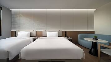A modern hotel room with a large bed, two bedside tables, a sofa, and a small round table.