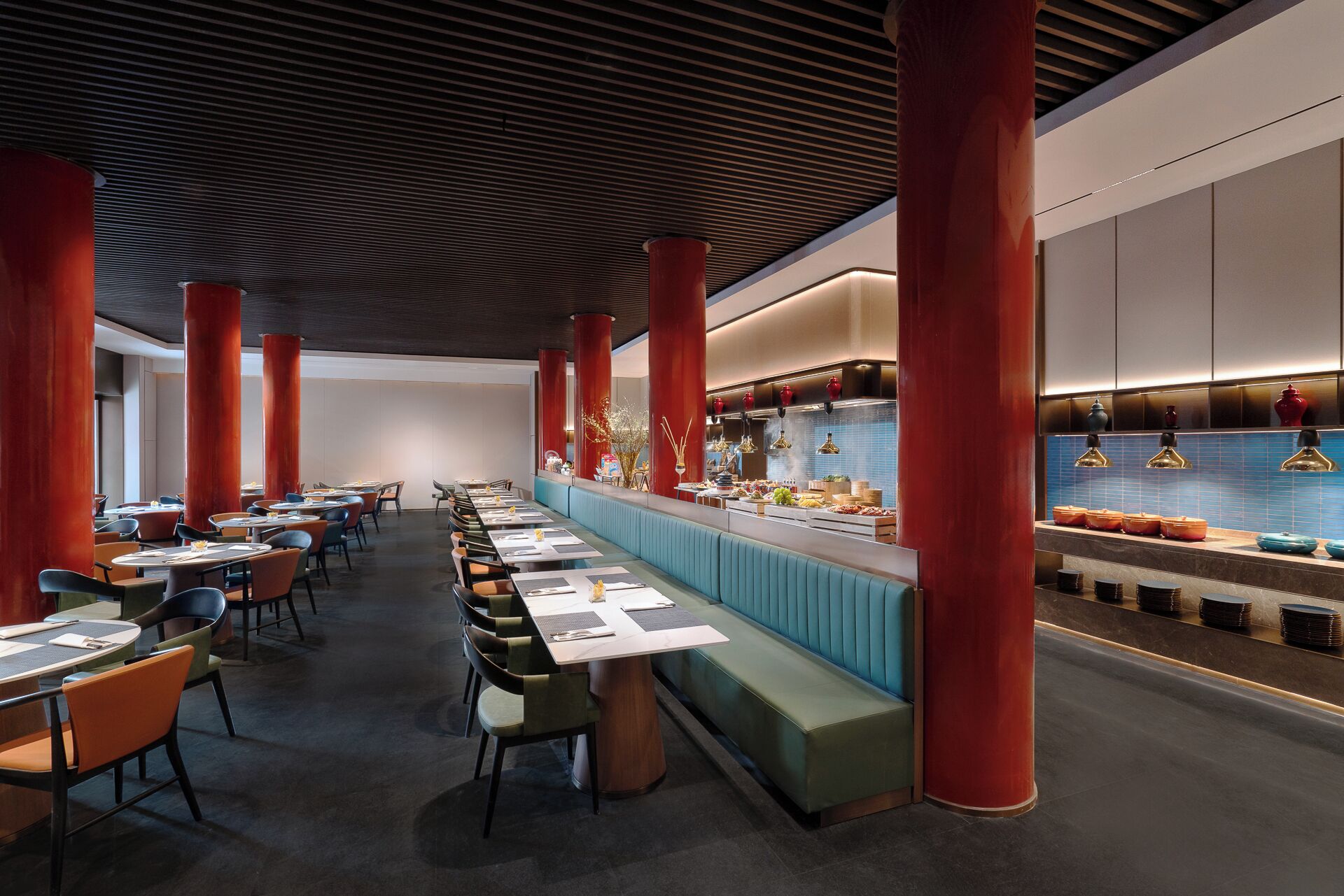 A modern restaurant with high ceilings, red columns, and a long counter with food displays.