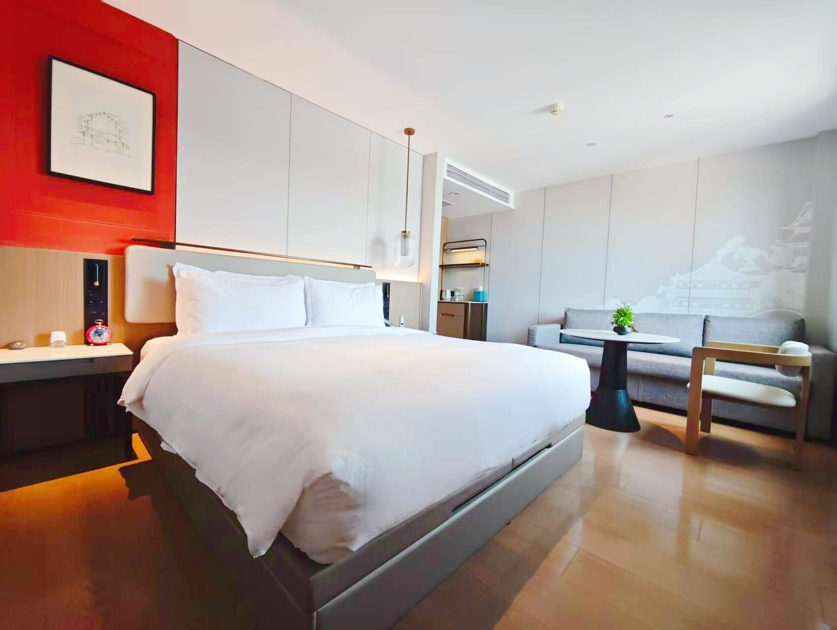 A modern hotel room with a large bed, a desk, a sofa, and a dining area.